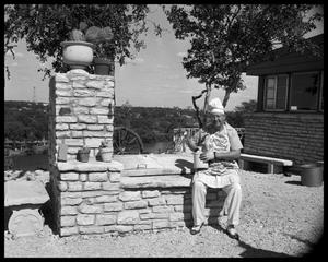 Primary view of object titled 'Dewey Bradford seated beside barbecue grill'.