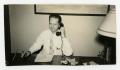 Photograph: [Man Sitting at Desk with Phone and Cigarette]
