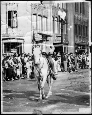 Primary view of object titled '[Photograph of C. M. "Pete" Frost riding on a white horse in a parade]'.
