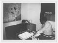 Photograph: [Two Persons Sit in an Office]