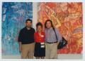 Photograph: [Photograph of Three People Standing in Front of Two Paintings]